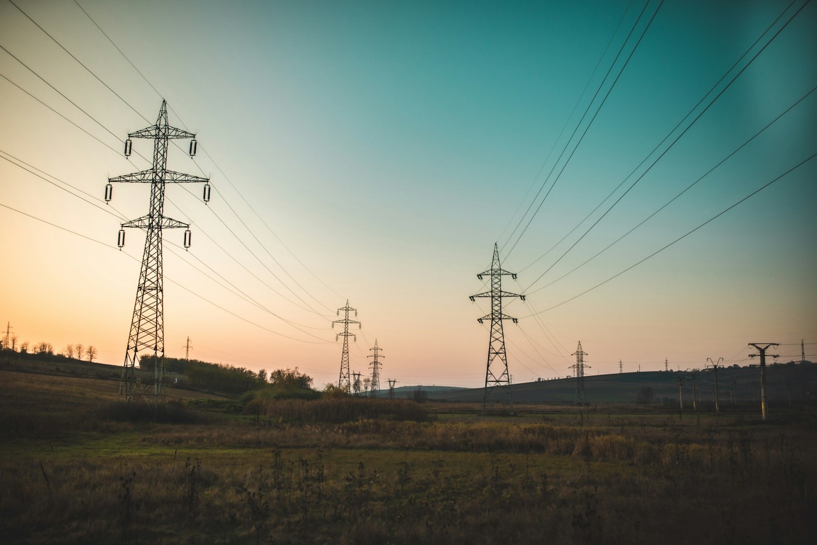 Transmission towers across open country under a pale morning sky
